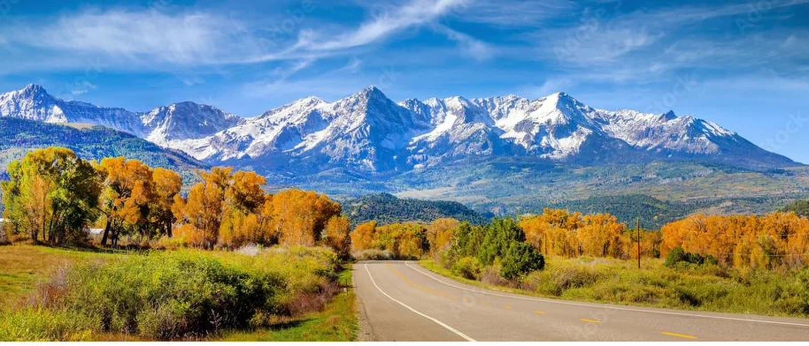 Snow-capped Colorado range above autumn aspens and a valley road